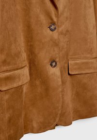 Bruine suède blazer met een gekleed kraag, twee voortassen en twee ronde knopen voor de sluiting. Soepele textuur met een subtiele glans.