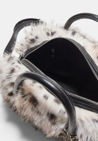 Borsa con manici in pelle nera e esterno in finta pelliccia bianca maculata, che mostra il compartimento principale con zip aperto e interno in tessuto nero.