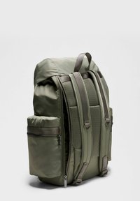 Zelena ruksak s podstavljenim mrežastim leđima, podesivim trakama, bočnim zip-zip zupčanikom i glatkim sintetičkim materijalom. Ima dizajn s zaobljenim vrhom.