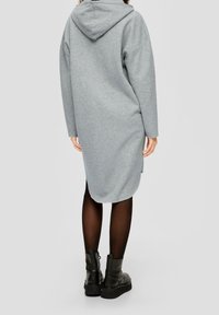 Vestido de sudadera gris con capucha, mangas largas y dobladillo ligeramente curvado. Llevado sobre unos leggings negros con botas negras gruesas.
