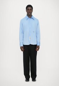 Lichtblauw overhemd met lange mouwen en een puntige kraag, met knoopsluiting, subtiele borduursels, gecombineerd met zwarte broek en schoenen.