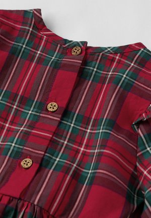 Tissu en carreaux rouges, verts et blancs avec un col rond et trois petits boutons marron sur le devant.