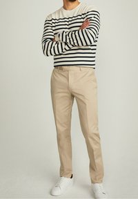 Maglione di cotone a righe in bianco e blu navy, abbinato a pantaloni beige e sneakers bianche. I pantaloni hanno una vestibilità classica con tasche.