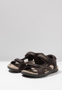 Bruna sandaler med öppen tå, Velcro-remmar, vadderad sula, texturerad yta och slitstark gummisula utformade för komfort och stöd.