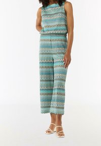 Combinaison sans manches présentant un motif ondulé en turquoise, beige et marron. Fabriquée en tissu lisse avec une coupe décontractée et des jambes larges.