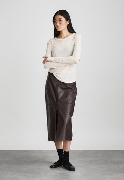 Top beige de manga larga con textura suave, combinado con una falda midi de cuero marrón que presenta detalles de costura y una abertura frontal. Calzado negro.
