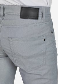 Jean en denim gris avec une poche arrière, une étiquette de marque en cuir à la taille et des détails de couture subtils.
