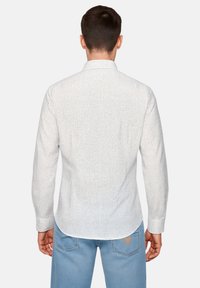 Camicia bianca a maniche lunghe con un piccolo motivo a pois neri, colletto standard e orlo curvo, abbinata a jeans di denim blu chiaro.