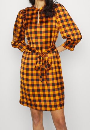 Checkered dress featuring orange and black squares, knee-length, with a keyhole neckline and a fabric belt at the waist. Textured sleeves.