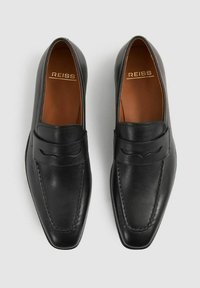 Svarta läderloafers med fyrkantig tå, tydlig sömnad och ett dekorativt band över ovandelen. Insidan har ett brunt foder.