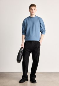 Ανοιχτό μπλε φούτερ με ριμπ λαιμόκοψη, μαύρο στενό παντελόνι με πλαϊνές τσέπες, μαύρη τσάντα και σκούρα παπούτσια. Ξεκάθαρες υφές ομαλού υφάσματος.