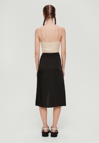 Beige geribbelde tanktop met dunne bandjes, gecombineerd met een vloeiende zwarte midi-rok. Zwarte blockheel sandalen maken de outfit af.