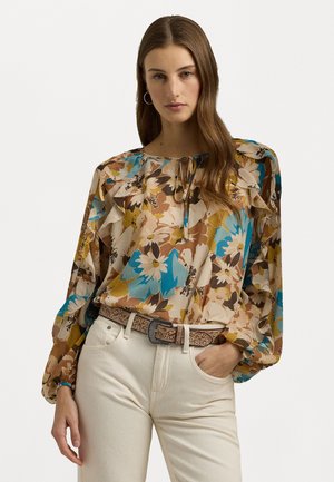 Flerfarget bluse med blomsterprint, lange pufferm, volang-syning ved halsen og knytedetalj, sammen med lyse bukser og et mønstrete belte.