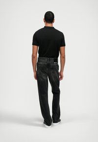 Polo preta com mangas curtas, combinada com jeans cinza escuro. Os jeans possuem um acabamento sutil e bolsos traseiros com detalhes de costura discretos.
