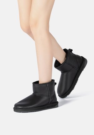 Black ankle boots made of leather with a soft fur lining, rounded toe, and a low rubber sole. Features a folded cuff and side stitching detail.