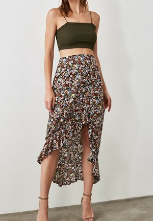 Jupe portefeuille florale avec ourlet inégal, base marron avec un imprimé floral coloré. Associée à un crop top ajusté vert. Détails à bords volants.