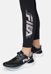 Svarta sportskor med blå accenter och en vit logotyp. Skorna har ett texturerat material och en vadderad sula. Svarta leggings med en vit grafisk detalj.