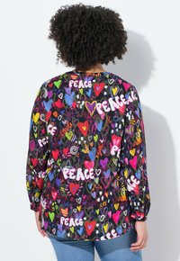 Langsleeve shirt met een zwarte achtergrond, versierd met meerkleurige harten en de tekst "PEACE", gemaakt van lichte stof met een ontspannen pasvorm.