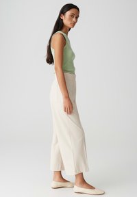 Lichtgroene mouwloze top, beige wijde broek en beige ballerina's; zachte textuur, eenvoudig ontwerp en op maat gemaakte pasvorm.