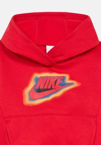 Felpa rossa con cappuccio in finitura testurizzata, caratterizzata da un logo centrale Nike in nero e arancione con dettagli blu. Include un cappuccio e una tasca frontale.