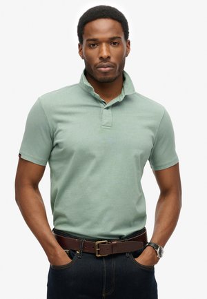 Kortærmet polo skjorte i blødt grønt stof med krave og tre knapper. Parret med et brunt læderbælte og mørke jeans.