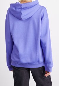 Fialová mikina s kapucí na stažení, vyrobená z měkké směsi bavlny. Má žebrované manžety a lem, a volný střih. Nosit s tmavými kalhotami.
