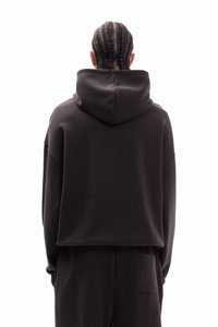 Crna skraćena dukserica od mekanog tkanja s kapuljačom na vezice, izraženim šavovima i opuštenim krojem, uparena s odgovarajućim hlačama koje imaju stražnji džep.