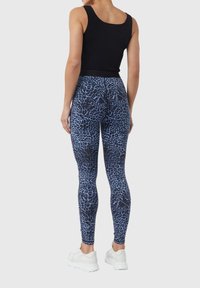 Leggings a vita alta in stampa leopardata nera e blu, in tessuto elastico e liscio, abbinati a un top nero e sneaker bianche.