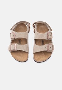 Μπεζ σουέντ σανδάλια Birkenstock με δύο λουριά με χαλκοκόκκινες αγκράφες και φελλό πάτο, σε λευκό φόντο.