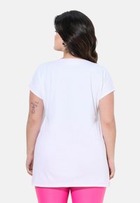 T-shirt bianco a maniche corte con cuciture di accento rosa, vestibilità comoda e design con parte posteriore più lunga. Il tessuto appare liscio e leggero.