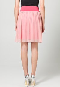 Gonna in tulle rosa con una ampia vita rosa, design a lunghezza ginocchio e texture stratificata, abbinata a scarpe col tacco alto argentate e lucide.