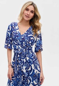 Niebieska sukienka w kwiatowy wzór z dekoltem w kształcie litery V i krótkimi faliście opadającymi rękawami, uszyta z lekkiego materiału, z przewiązanym w pasie i zwiewnym dołem.