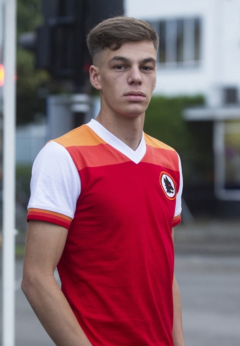 Rode voetbalshirt met oranje verloopmouwen, witte kraag en een logo op de linkerborst. Korte mouwen en een slim-fit design.