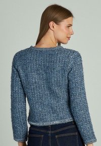 Maglione blu lavorato a maglia con una finitura testurizzata, di lunghezza cropped e maniche lunghe. Presenta un collo rotondo e un leggero luccichio lungo l'orlo.