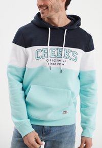 Bluza z kapturem w kolorze granatowym, białym i akwamarynowym z kieszenią kangurkową. Posiada wyraźny napis "CREEKS" oraz teksturowane wykończenie. Regulowane sznurki.