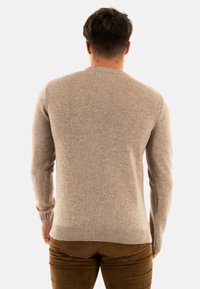 Pull en maille beige à manches longues et col rond. La texture est douce et semble chaude, associé à un pantalon en velours côtelé vert olive.