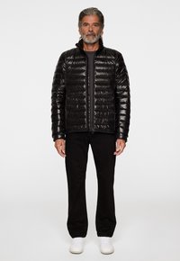 Svart puffjacka med quiltat mönster, hög krage och hel dragkedja; kombinerad med svarta byxor och vita sneakers.