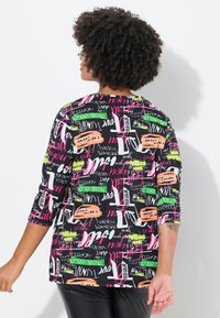 Musta pusero, jossa on kirkasta graffitotyylistä tekstiä vaaleanpunaisissa, vihreissä ja oransseissa sävyissä. Kolme neljäsosaa hihat ja rento istuvuus.