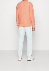 Pull corail avec un tricot texturé, coupe ample, col rond et poignets côtelés, associé à un jean bleu clair et des baskets blanches.