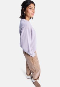 Felpa viola chiaro con scollatura arrotondata e polsini a costine; abbinata a pantaloni beige a vestibilità comoda e pantofole beige. Design semplice e casual.