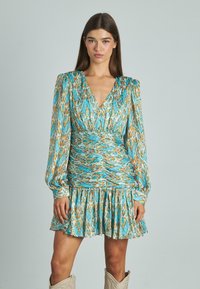 Vestido cruzado floral con mangas largas abullonadas. Presenta un patrón en teal, naranja y blanco, escote en V, cintura fruncida y dobladillo con volantes.