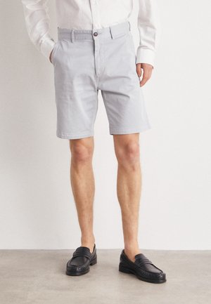 Jasnoszare bawełniane szorty z płaskim przodem, bocznymi kieszeniami i zapięciem na guzik, w zestawieniu z czarnymi wsuwanymi mokasynami.