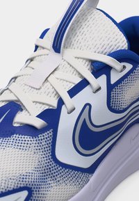 Κοντινό πλάνο λευκού και μπλε αθλητικού παπουτσιού με άνω μέρος από δίχτυ, λευκά κορδόνια και λογότυπο Nike στη πλευρά.