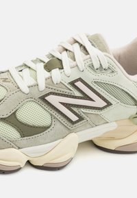 Limegrønn semsket og mesh sneaker med hvite lisser, en fremtredende brun "N"-logo og en teksturert gummisåle med beige detaljer.