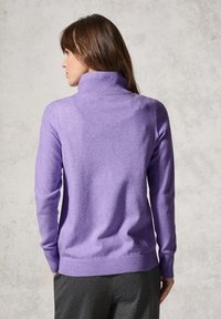 Pull en maille violet clair avec un col montant, des poignets et un ourlet côtelés. Texture lisse ; design ajusté, montrant la vue arrière, porté avec un pantalon sombre.