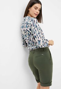 Blusa con motivi di foglie multicolori in tonalità pastello; pantaloni corti verde oliva aderenti con orli arrotolati, parte anteriore piatta e tasche posteriori.