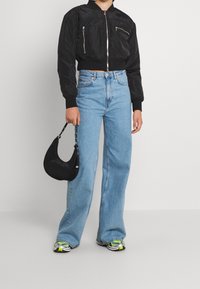 Black cropped bomber jacket with zip pockets, light blue high-waisted jeans, black handbag, and athletic shoes with green accents.