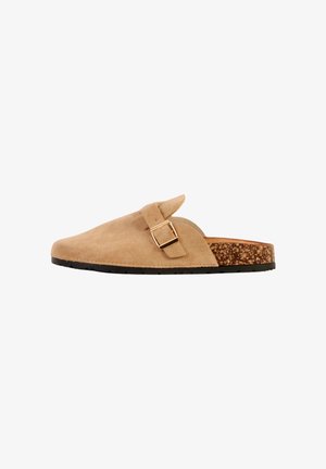 Beige suède instapslof met gouden gespsluiting, kurken sleehak en zwarte rubberen zool, zijaanzicht.