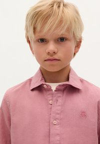 Lys pink button-up skjorte lavet af tekstureret stof, med krave og en broderet kranielogo på brystet, samt lyse knapper.