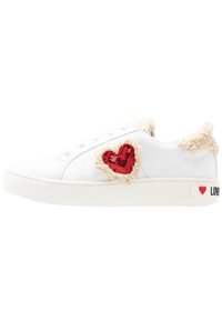 Vit lädersneaker med fluffiga beige detaljer och en röd paljetthjärta-applikation. Utrustad med en vit sula och tryckt detalj med texten 'LOVE'.